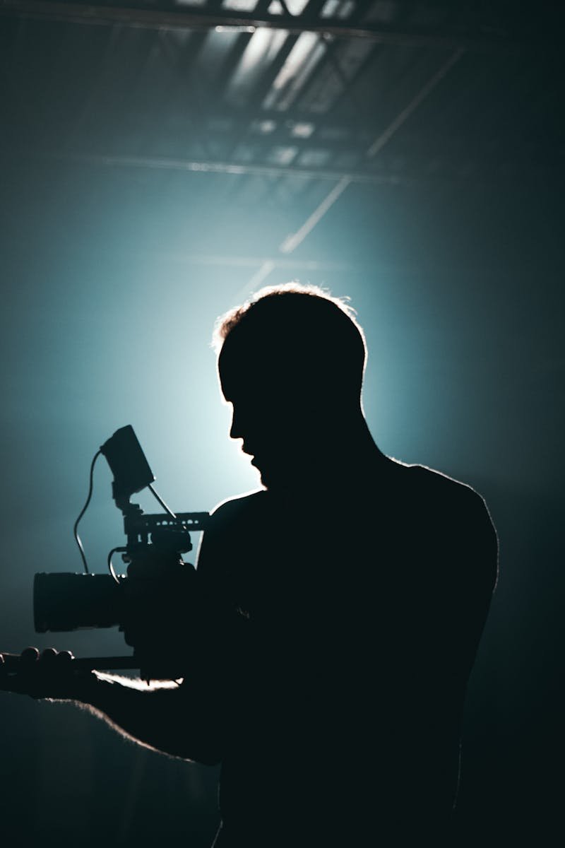 Silhouette of a cinematographer with camera gear in a dramatic, low light setting.